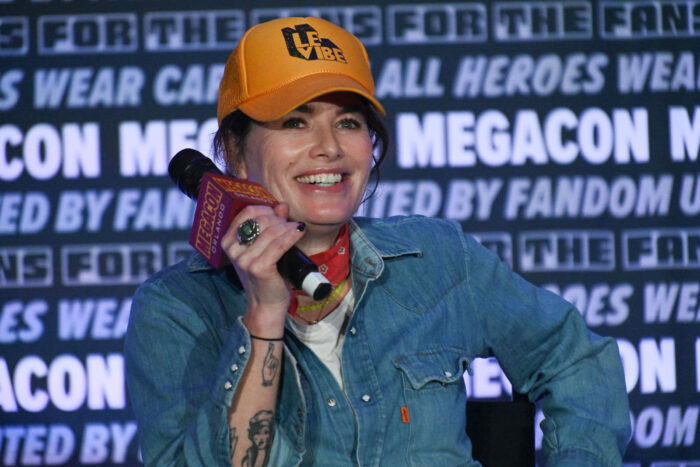 Actress Lena Headey smiling with a microphone at a Megacon event, discussing avoiding exposing herself. Actress Lena Headey smiling with a microphone at a Megacon event, discussing avoiding exposing herself.