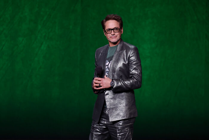 Robert Downey Jr. on stage, wearing a metallic silver suit, discussing superhero movies. Robert Downey Jr. on stage, wearing a metallic silver suit, discussing superhero movies.