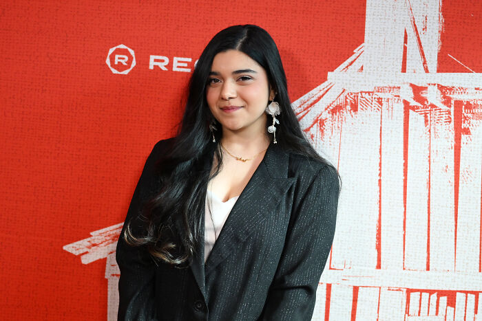 A young woman with long dark hair, wearing a black blazer and white top, poses for a photo. A young woman with long dark hair, wearing a black blazer and white top, poses for a photo.