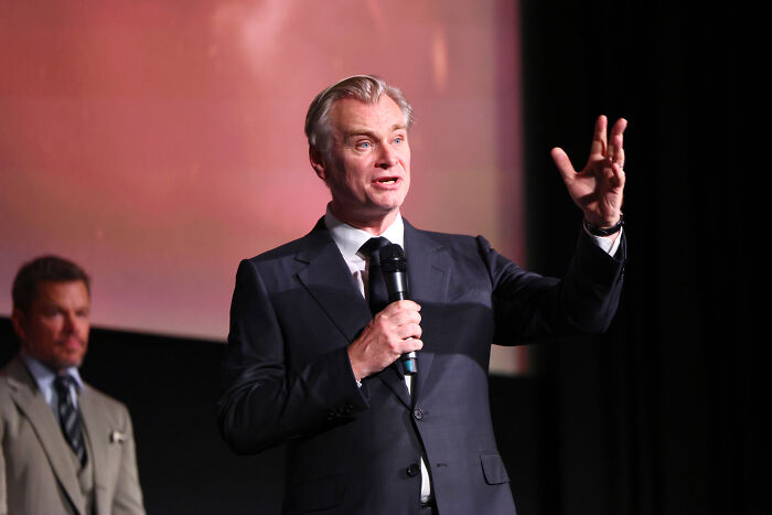 A man in a suit speaks into a microphone, gesturing with one hand, concerning the Age Gap in The Odyssey and Hollywood practice. A man in a suit speaks into a microphone, gesturing with one hand, concerning the Age Gap in The Odyssey and Hollywood practice.