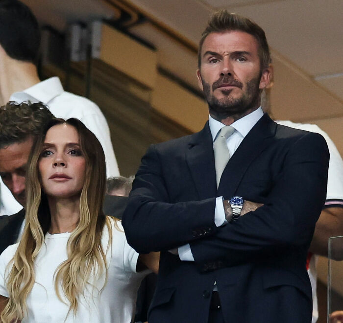 Victoria Beckham looking away as David Beckham crosses his arms, depicting their behavior. Victoria Beckham looking away as David Beckham crosses his arms, depicting their behavior.