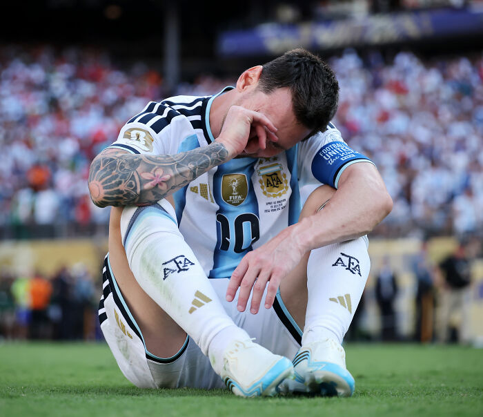 Lionel Messi sitting on the field, covering his face in disappointment during the World Cup Final. Lionel Messi sitting on the field, covering his face in disappointment during the World Cup Final.