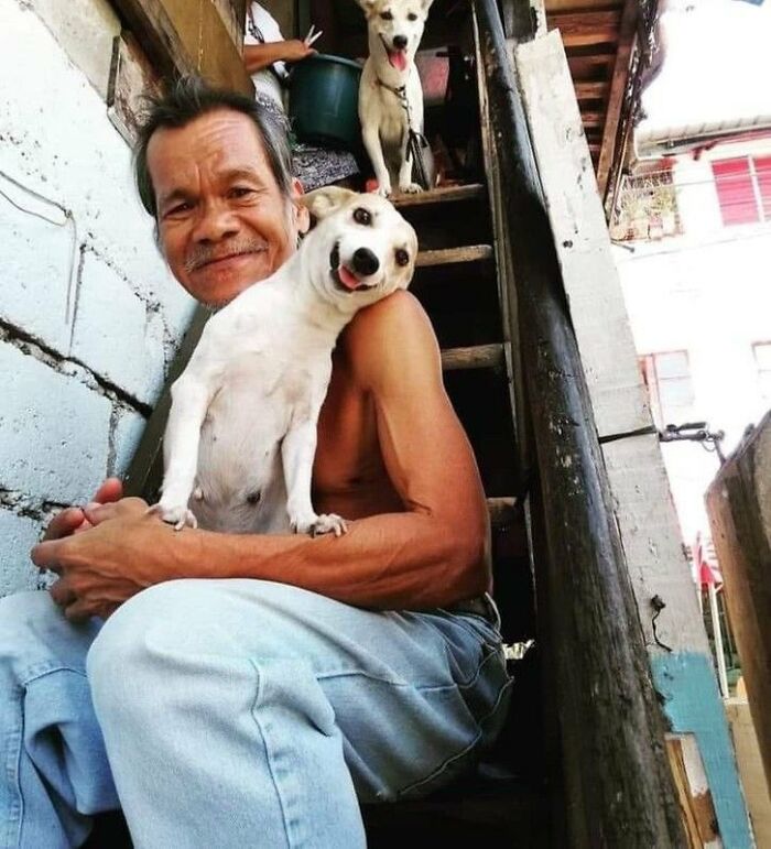 A man with a silly animal, a white dog, on his shoulder, and another silly animal, a white dog, on the stairs above.