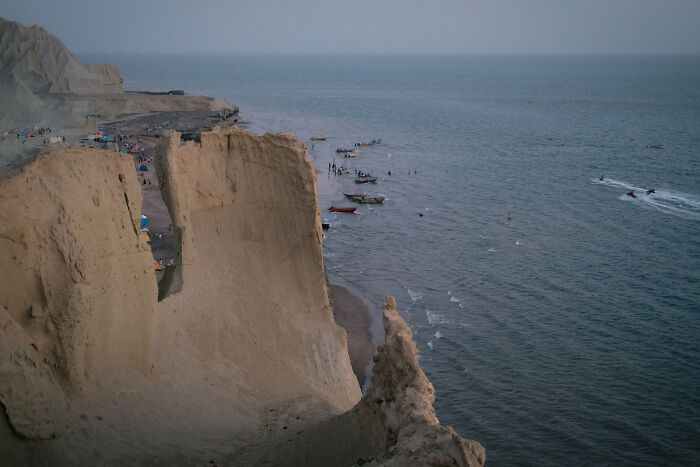 A high-angle view of the Strait of Hormuz showing a cliffside beach with boats and people enjoying the water.