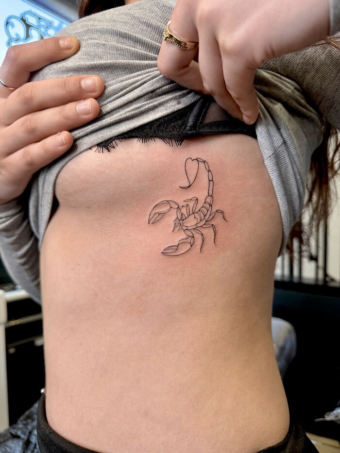 Minimalist scorpion tattoo design on the side of a body. Professional tattoo artist applies delicate lines.