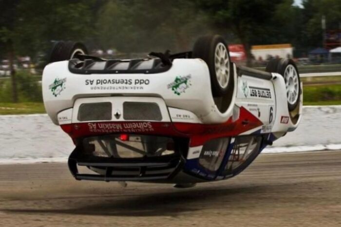 A white and red race car is upside down on a dirt track, a hilarious photo taken moments before disaster struck.