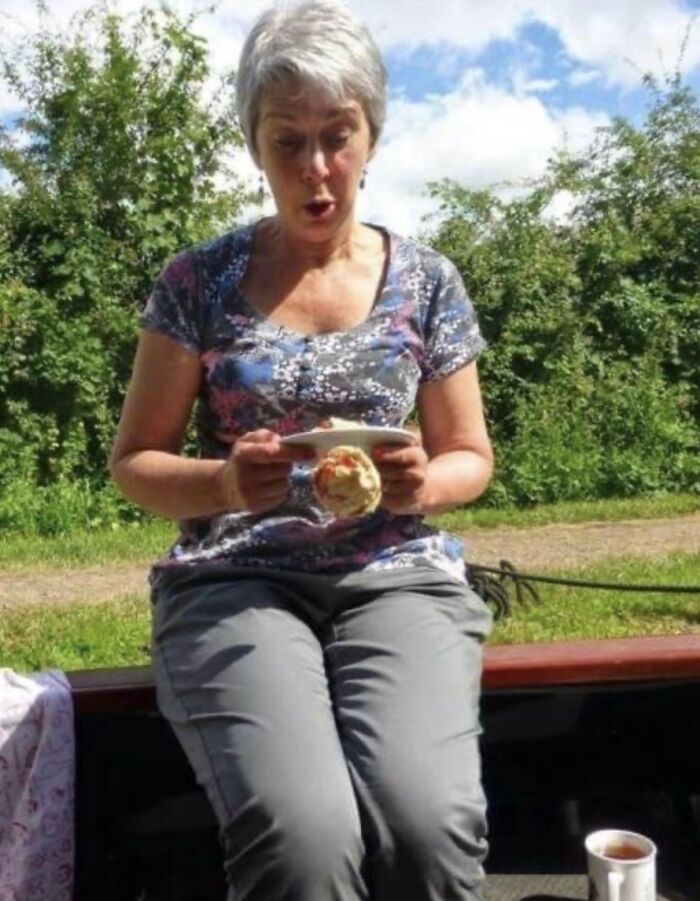 A woman with short gray hair looks shocked as a pastry falls from a plate, a moment before disaster.