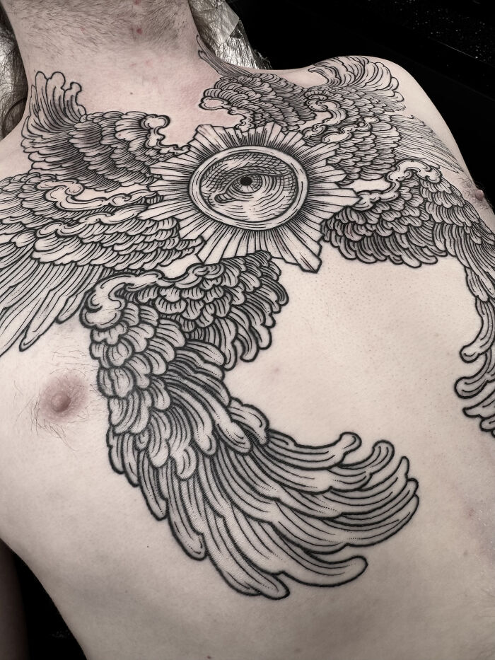 Intricate chest tattoo featuring an eye with wings. Professional tattoo artist crafts detailed and symbolic artwork.