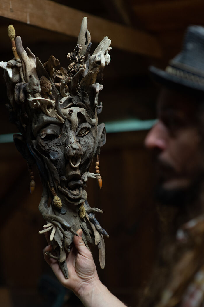 An artist holding a stunning wood sculpture of a screaming face, crafted from natural wood pieces with intricate details.