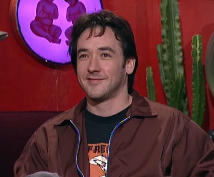 John Cusack smiling, reflecting on why he vanished from Hollywood and sister Joan's long absence.