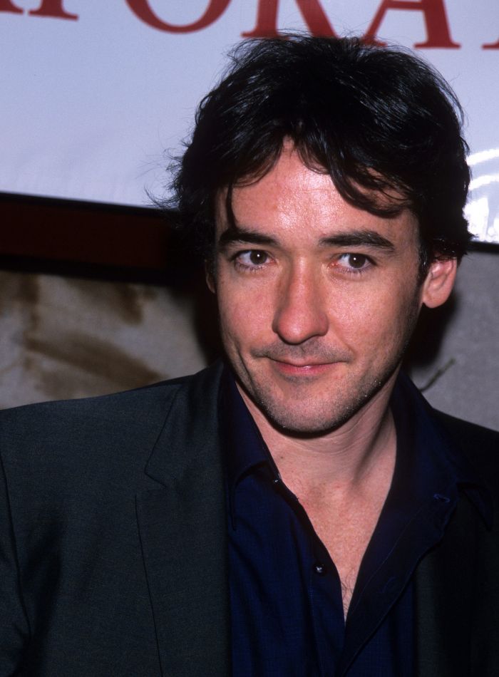 Young John Cusack in a dark suit, reflecting on his vanishing from Hollywood and sister Joan's absence.
