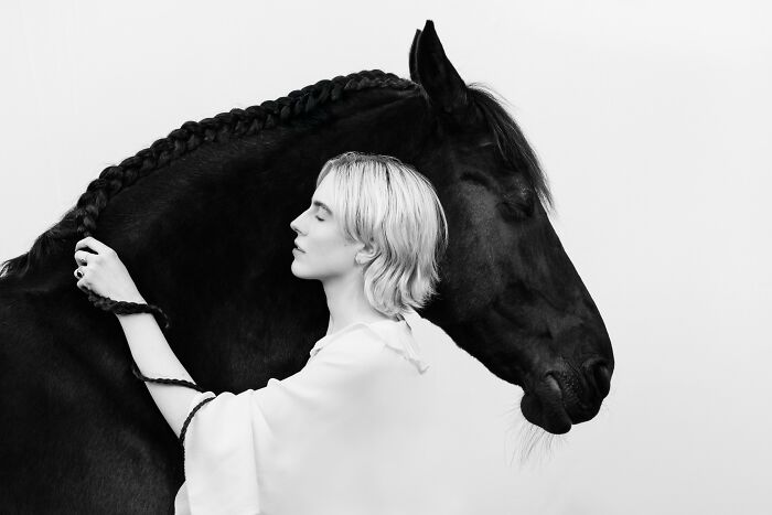 A black and white portrait of a woman gently touching the braided mane of a horse, from the Pet Photography Awards.