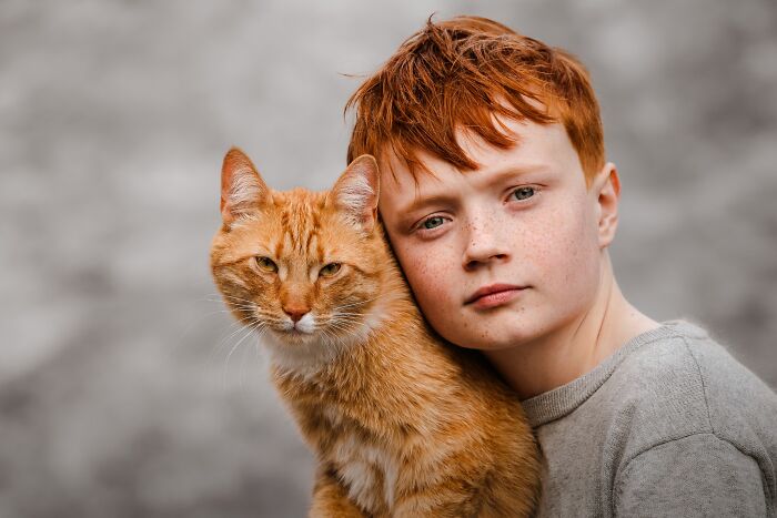 A young boy with red hair and freckles poses with an orange cat in a winning image from the Pet Photography Awards.