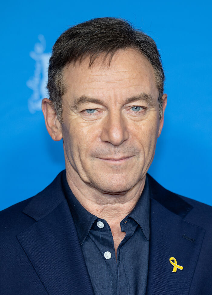 A man in a dark blue suit jacket and shirt, with a yellow ribbon pin, representing favorite celebrities.