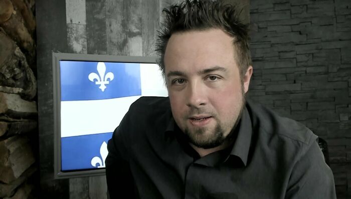 A man with spiky hair looking at the camera, with a flag in the background, relating to unsolved mysteries.