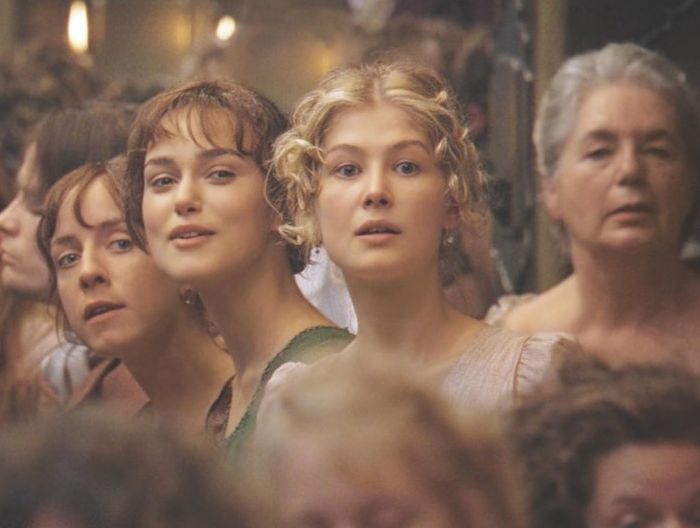 Keira Knightley and Rosamund Pike in a movie scene, looking forward amidst a crowd of people.