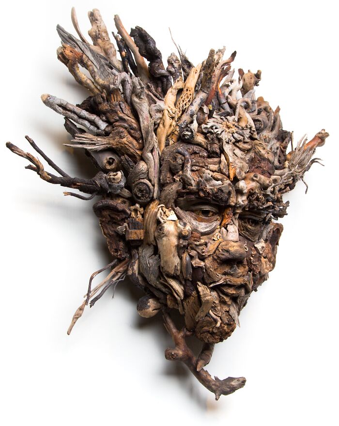 Intricate wood sculpture of a face and head, crafted from collected natural wood pieces, with a dark eye and textured surface.