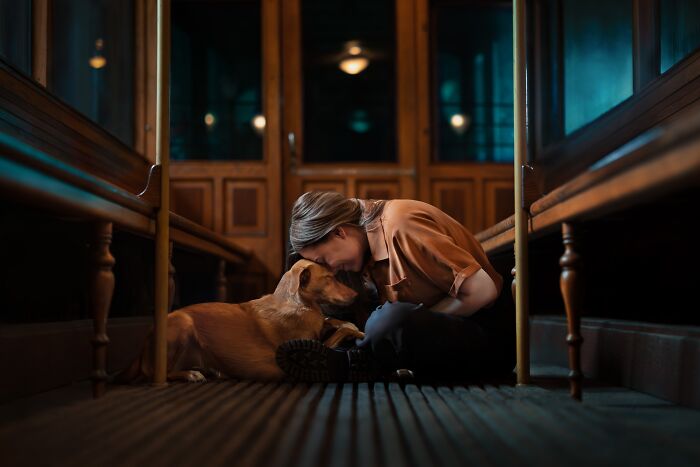 A woman kneels, embracing a dog in a warm, dimly lit hallway, an entry in the Pet Photography Awards.