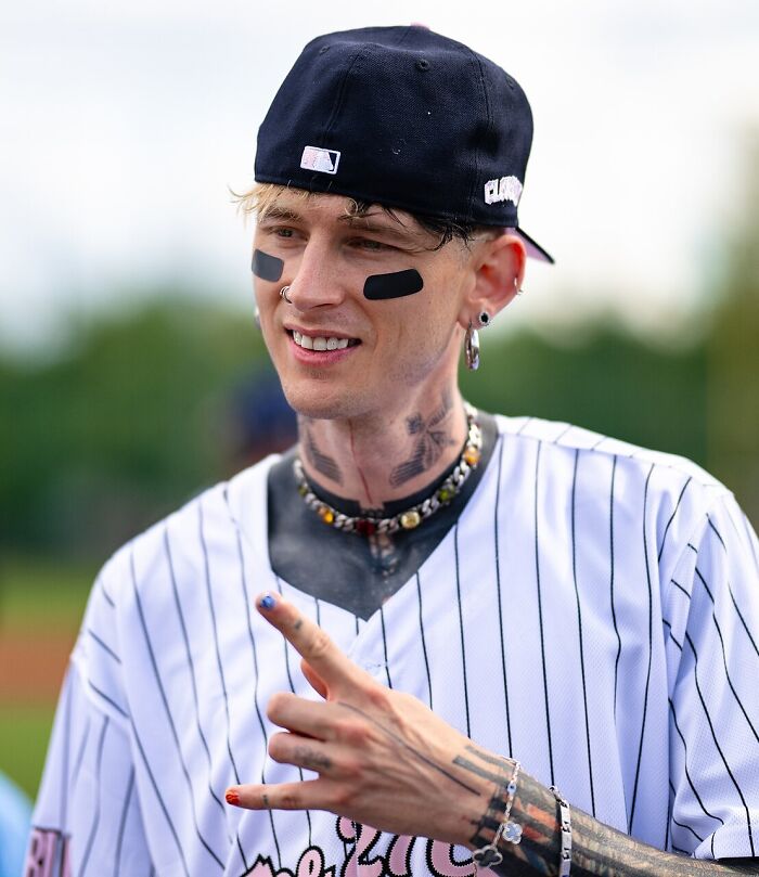 Machine Gun Kelly with face paint and tattoos, looking at the camera, showing a disillusioned celebrity.