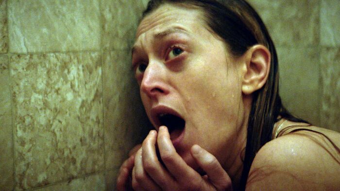 A frightened woman with wet hair and a desperate expression from a terrifying horror movie.