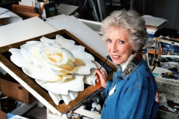 An elderly woman painting a large white rose, revealing fascinating things about the world.