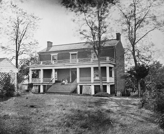 A black and white image of a historic brick house with a porch and steps, full of untold history facts.