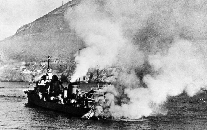 A black and white photo showing a warship on fire in the water, a significant history fact.