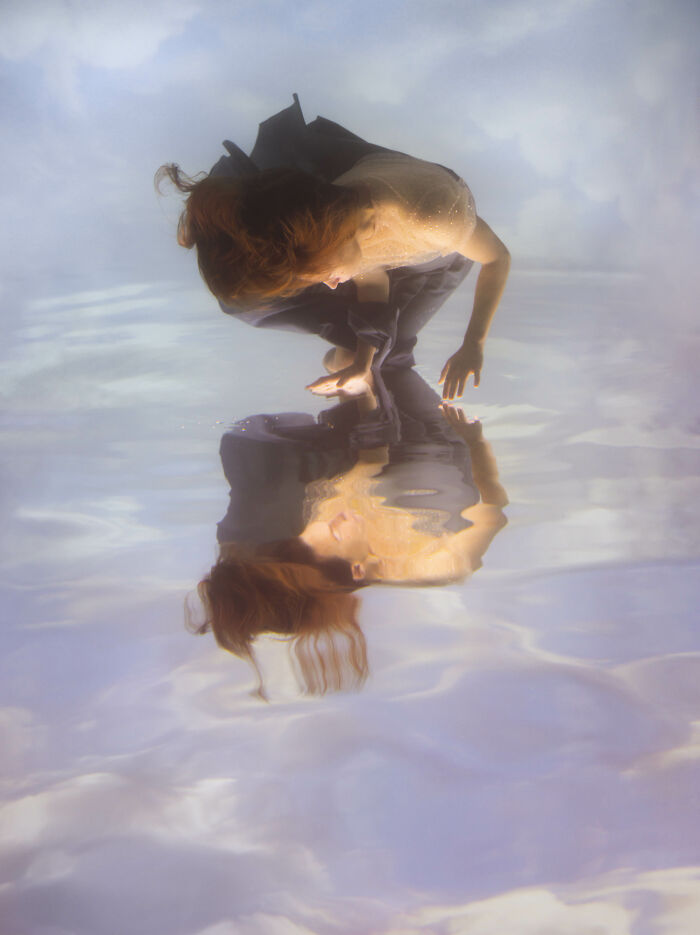 A woman creates surreal photos by submerging herself in water, bending over to touch her reflection.