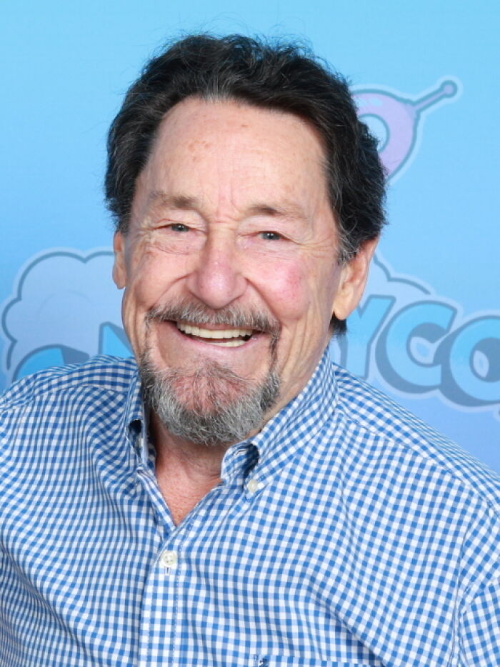 A smiling older man with a beard and checkered shirt, sharing fascinating things about the world.