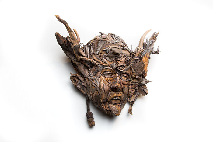 Expressive wood sculpture of a face with horn-like elements, composed of collected pieces of wood.