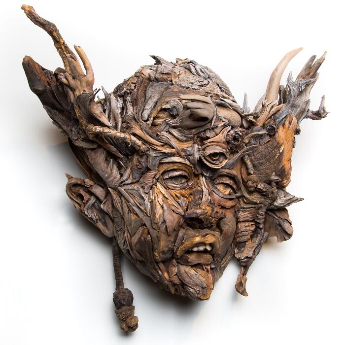 Expressive wood sculpture of a face with horn-like elements, composed of collected pieces of wood.