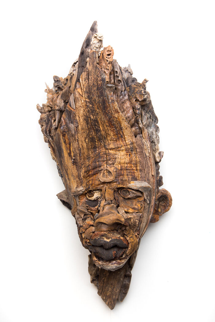 Unique wood sculpture featuring a expressive face with detailed features, made from collected pieces of wood.