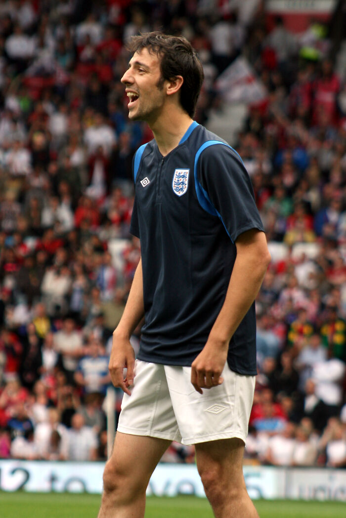 A male soccer player in a blue and white jersey on a field, smiling, as if a favorite celebrity.