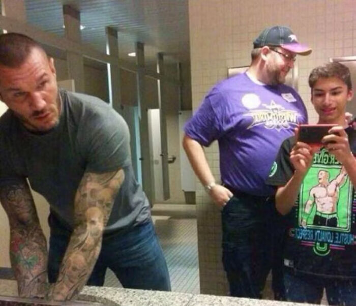A fan attempts to take a photo with a celebrity, Randy Orton, in a public restroom.