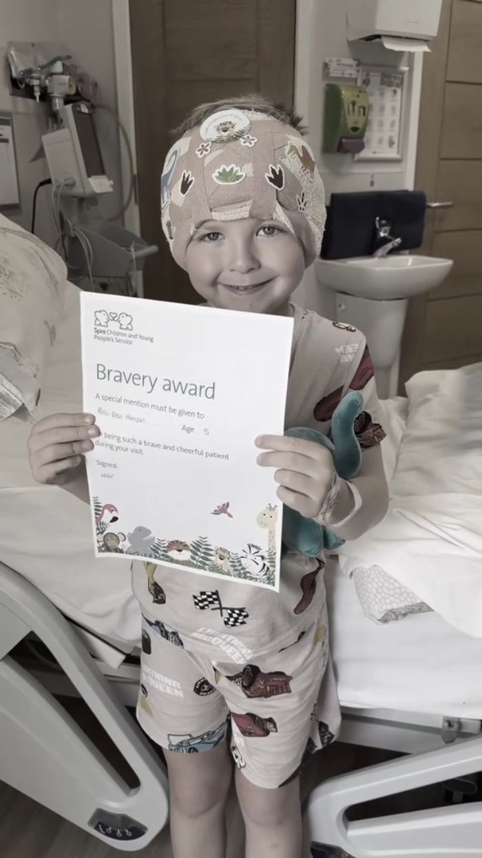 A smiling 5YO boy in a hospital bed holds a bravery award after his cosmetic surgery. A smiling 5YO boy in a hospital bed holds a bravery award after his cosmetic surgery.