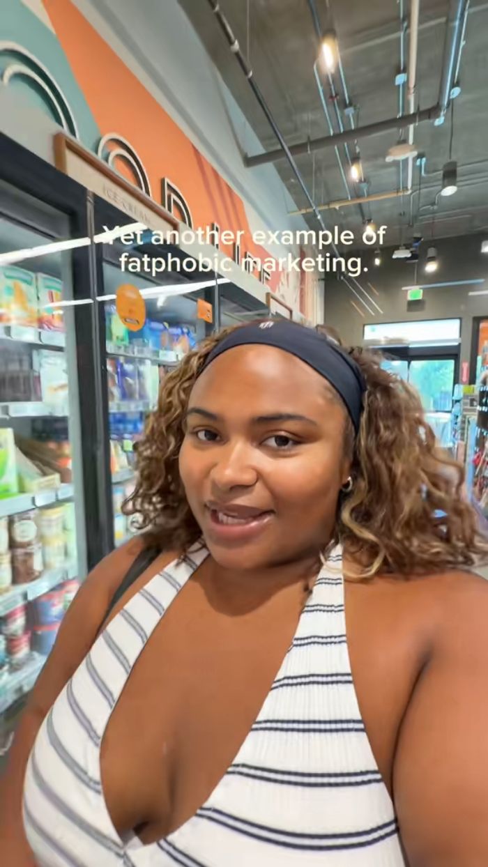 A plus size activist in a striped top, filming a video in a grocery store, calling out fatphobic brands. A plus size activist in a striped top, filming a video in a grocery store, calling out fatphobic brands.