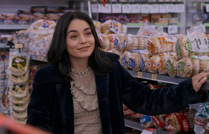 A smiling woman with dark hair in a grocery store aisle, looking sideways, perhaps feeling disillusioned by celebrities.