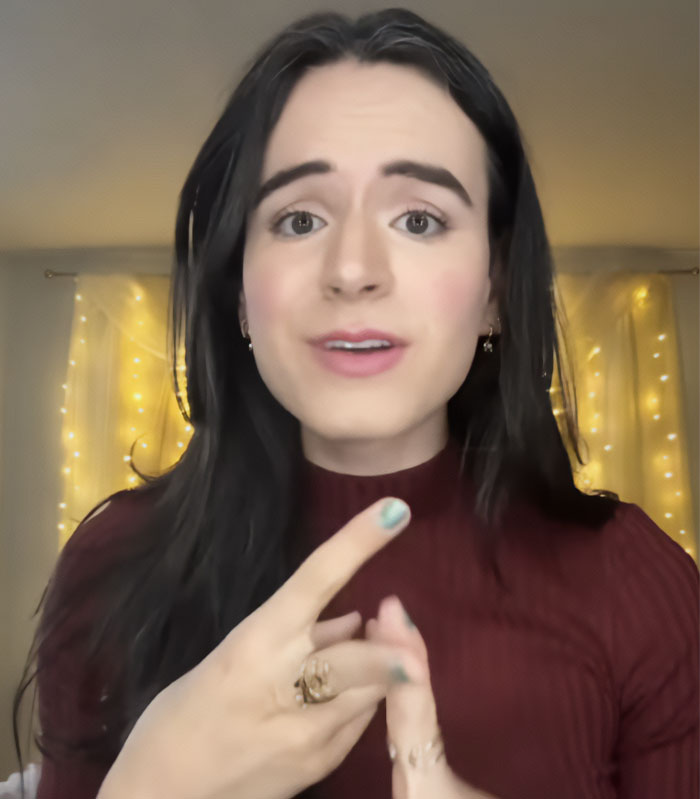 Close-up of a Trans Influencer with long dark hair and red top, gesturing, speaking about Lindsey Graham.