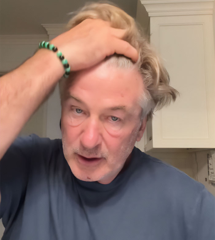 Alec Baldwin in a blue shirt, with a serious expression, raising a hand to his blonde hair, reacting to a Sam Neill tribute. Alec Baldwin in a blue shirt, with a serious expression, raising a hand to his blonde hair, reacting to a Sam Neill tribute.