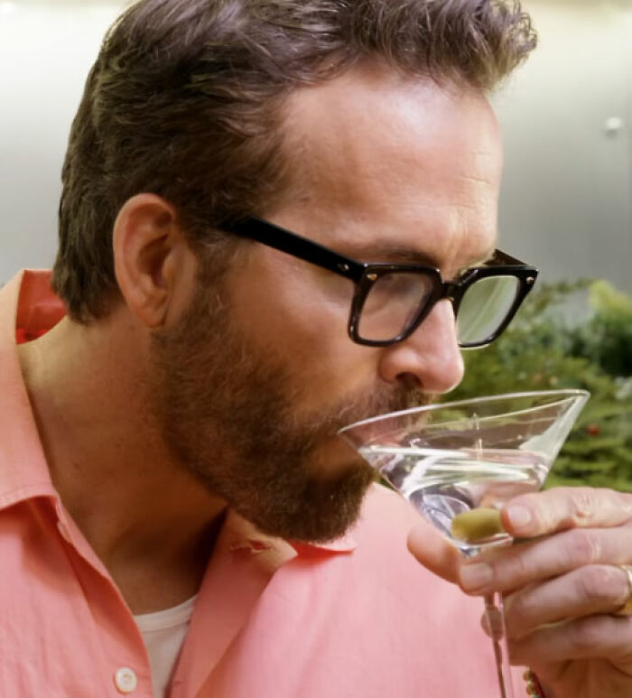 Ryan Reynolds with glasses, sipping a drink, unaffected by Hollywood backlash and not blacklisted.