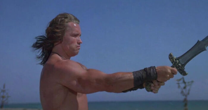 A muscular man with long hair, holding a sword against a blue sky, displaying fascinating things about the world.