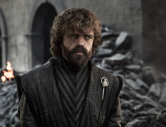 A male celebrity with curly hair and a beard, wearing a dark, textured tunic with a hand-shaped brooch. Favorite celebrities can disillusion fans.