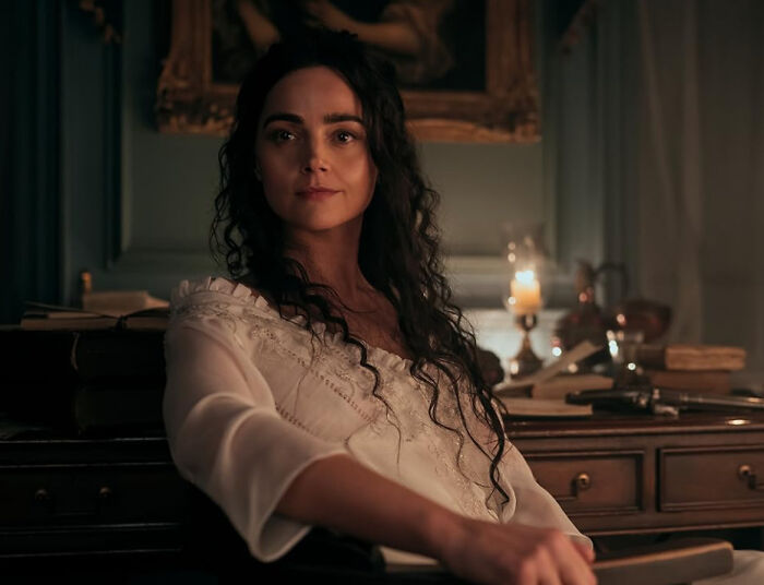A woman with long dark hair, wearing a white ruffled top, looking at the camera, conveying disillusionment by favorite celebrities.