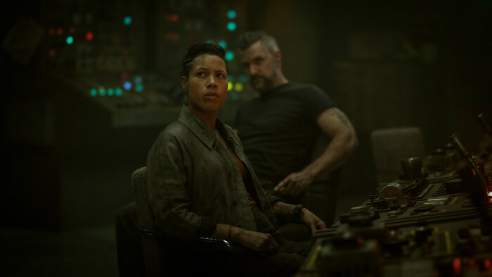 Two characters, part of the Silo Season 3 cast, in a control room, looking intently at something off-screen. Two characters, part of the Silo Season 3 cast, in a control room, looking intently at something off-screen.