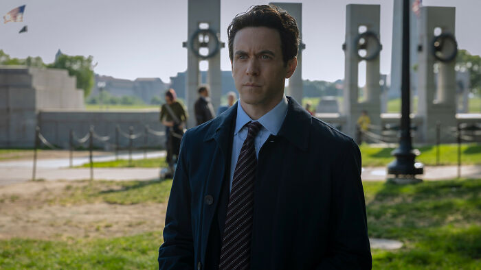 A pensive man in a suit, a returning Silo Season 3 cast member, stands outdoors looking into the distance. A pensive man in a suit, a returning Silo Season 3 cast member, stands outdoors looking into the distance.