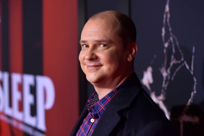 A man with a bald head and a blue plaid shirt, smiling at a Hollywood event. A man with a bald head and a blue plaid shirt, smiling at a Hollywood event.