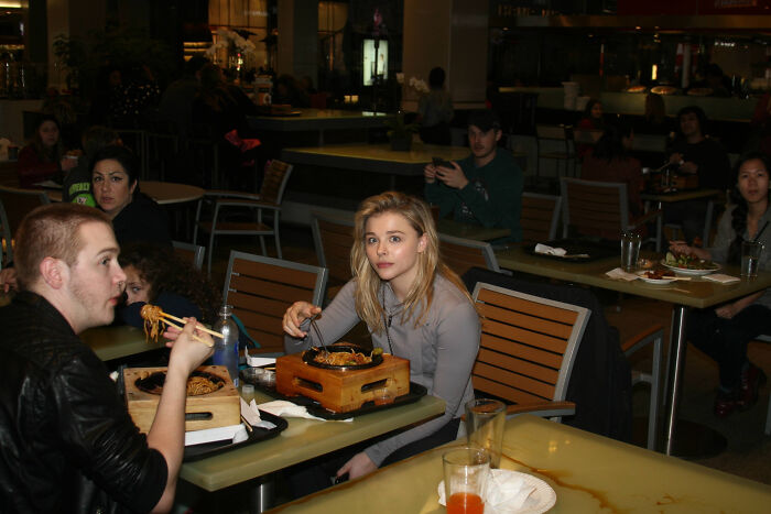 Chloë Grace Moretz, a celebrity, looks directly at the camera while eating, seemingly annoyed by a photo request.