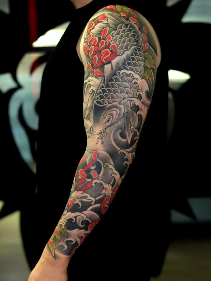 Colorful Koi fish and waves tattoo art covering a person's arm, an inspiring example of tattoo art.