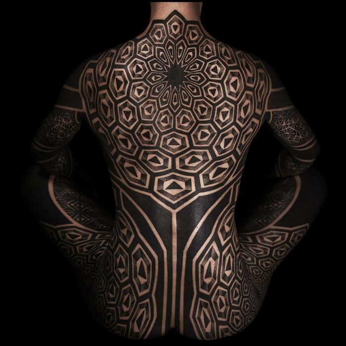 Geometric full-body tattoo art in black on a person's back and limbs, an inspiring example of tattoo art.