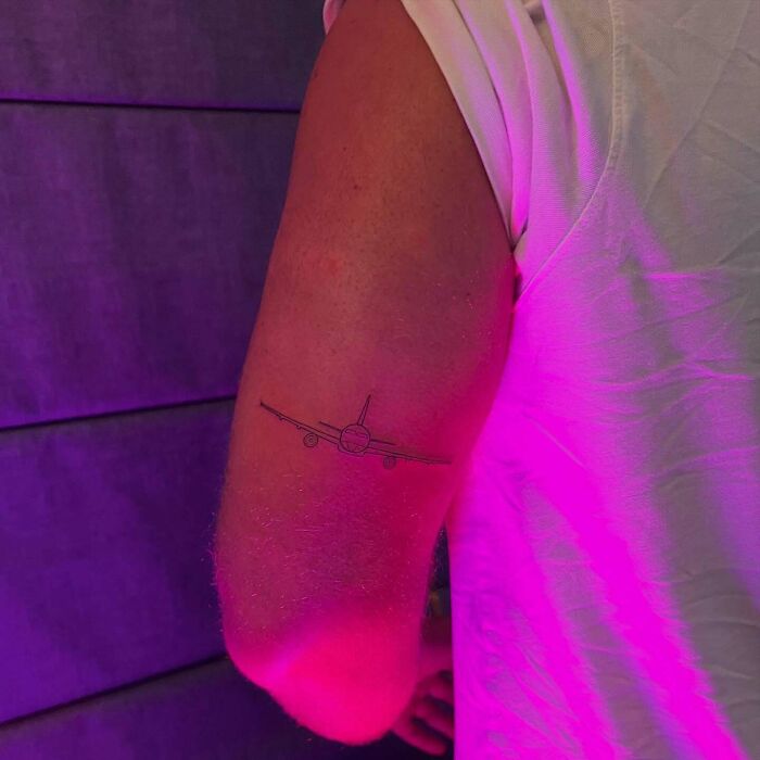 Minimalist airplane tattoo art on a person's upper arm, an inspiring example of tattoo art.